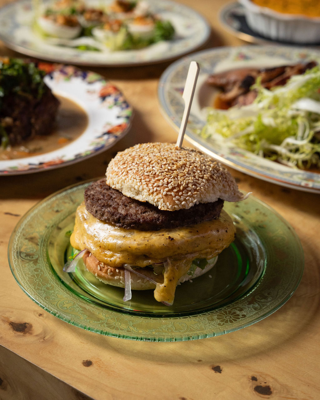 Cheeseburger on a sesame bun with melted cheese, served on green glass